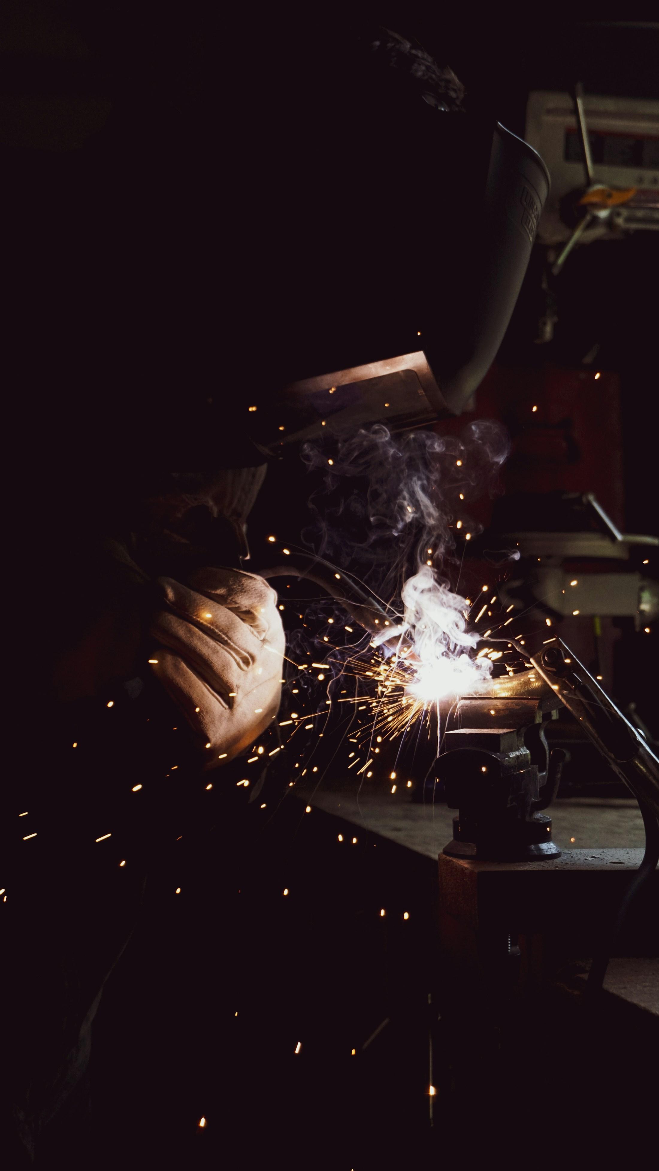 Welder joining a metal component as sparks fall through the workshop