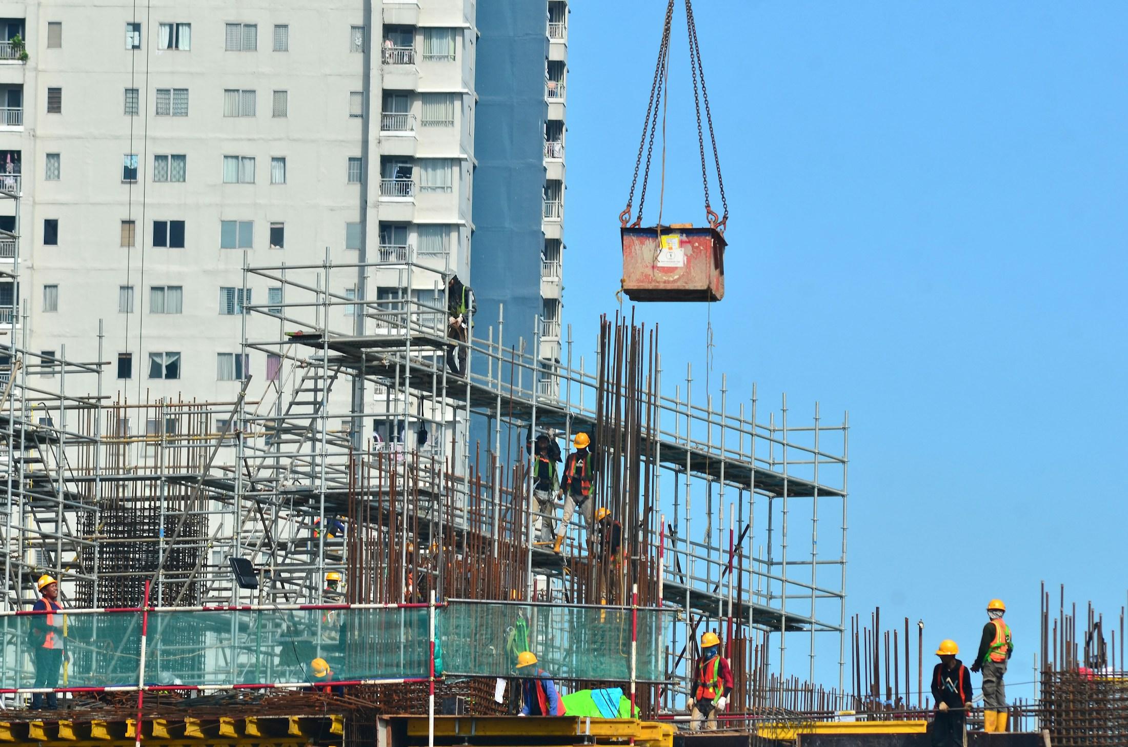 Construction workers on a scaffolded concrete deck beneath a suspended crane load